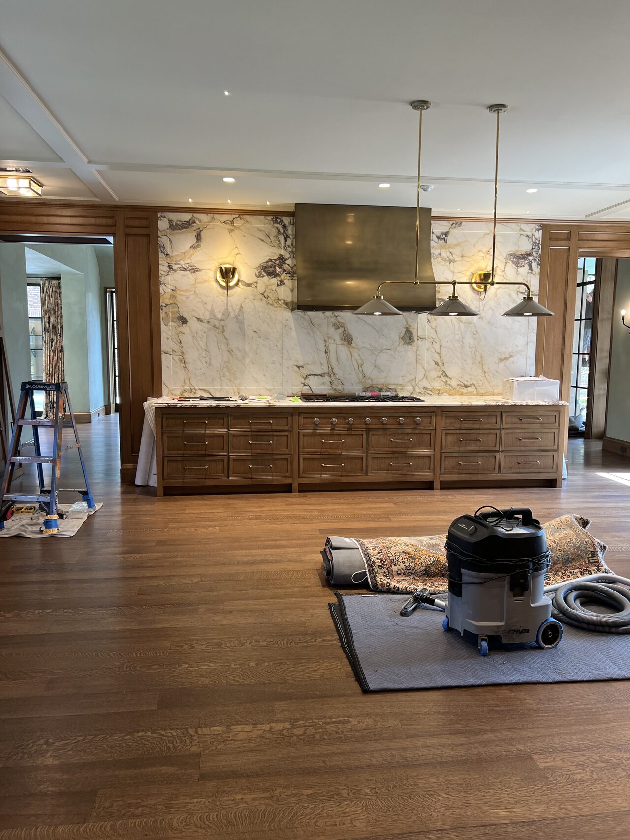 Wide kitchen view showing premium wood base cabinets, island work area, and hood wall finish coordination for a Joel Hodge project.