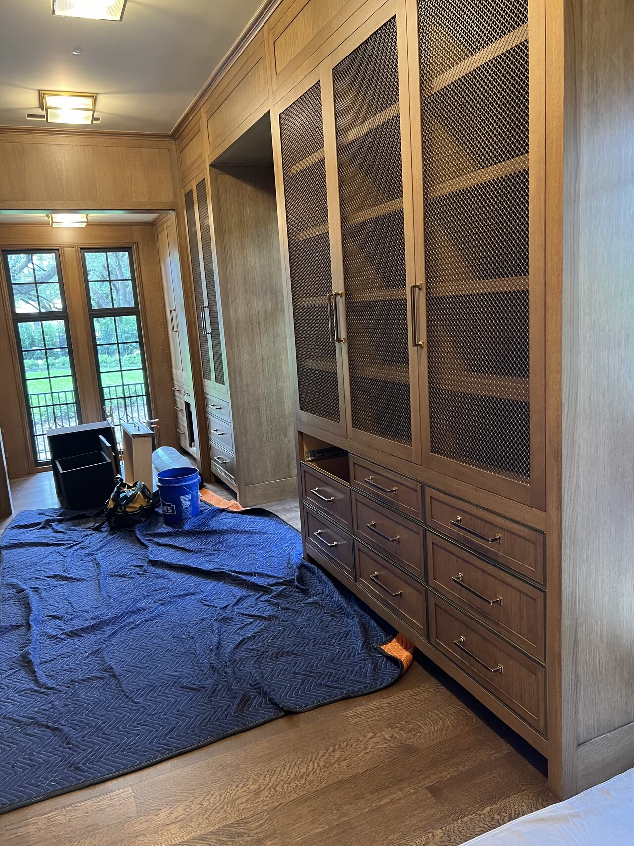 Tall wood cabinetry and panel wall being installed with floor protection and tools staged in the room for a Joel Hodge project.
