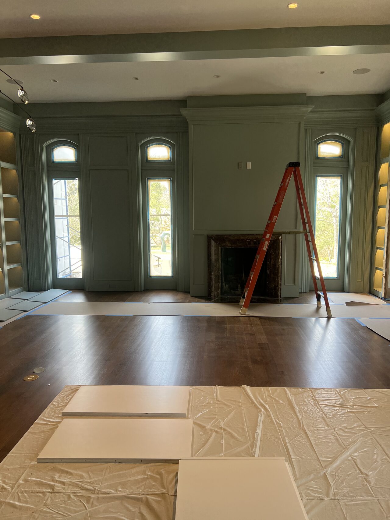 Room view before final media wall setup, showing entry doors, ceiling detail, and protected flooring for a Joel Hodge project.