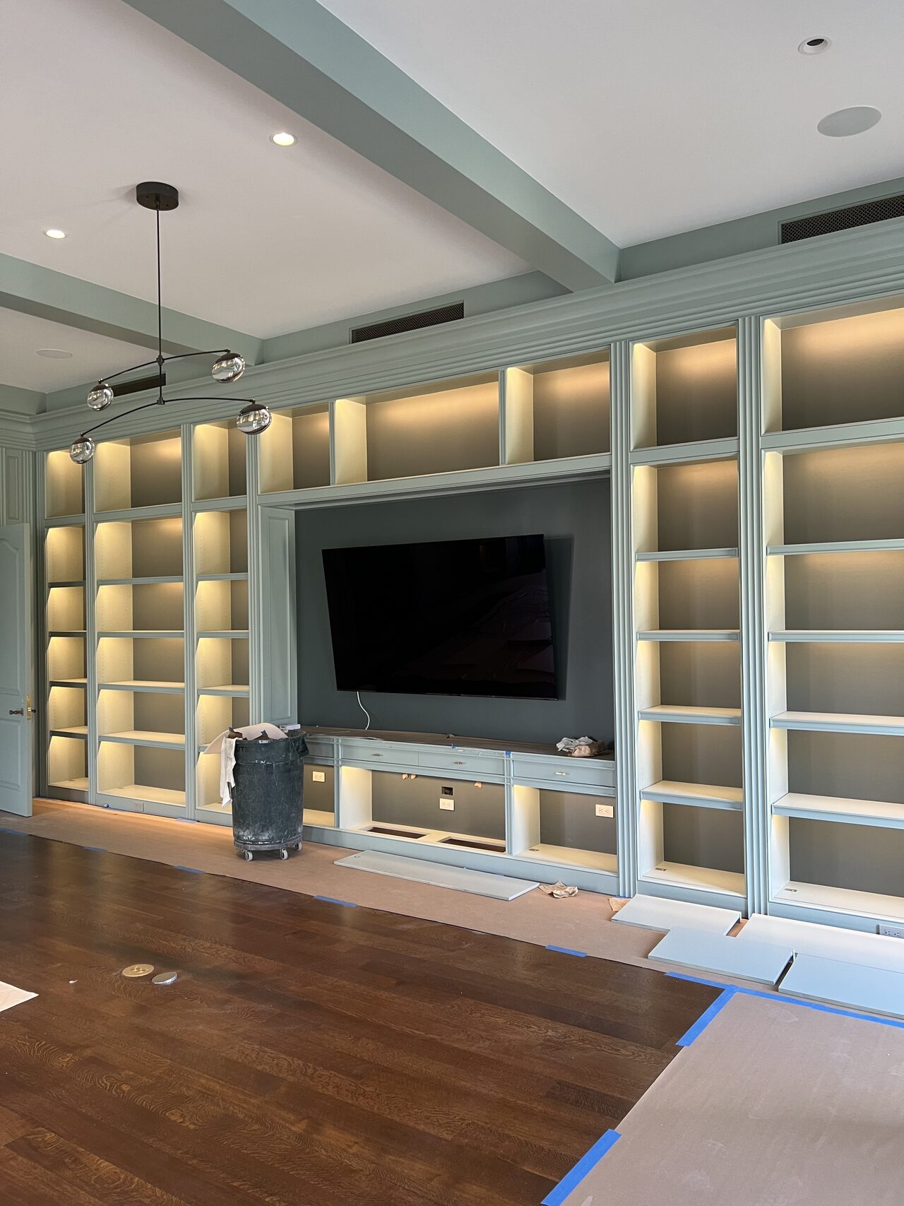 Completed media wall with TV opening, lit shelving, lower storage, and side display towers for a Joel Hodge project.