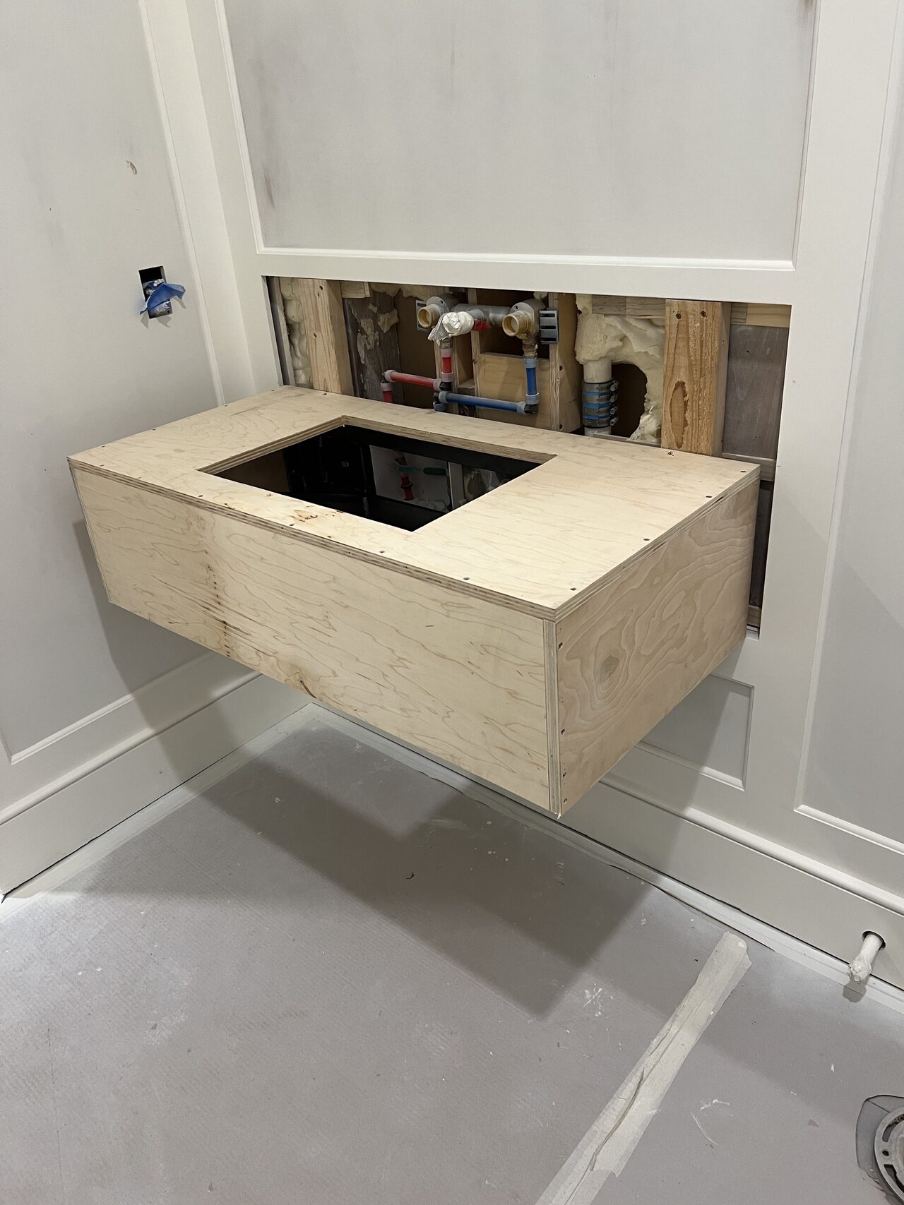 Small wall-hung vanity cabinet set around plumbing before countertop and final finish were added for a Joel Hodge project.