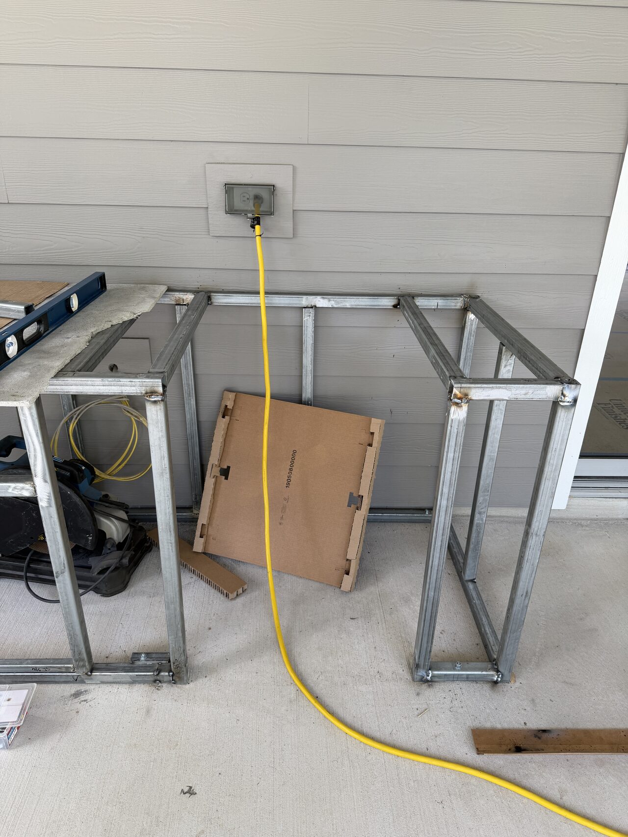 Patio-side metal frame section staged near the wall with tools and power access visible for a Joel Hodge project.