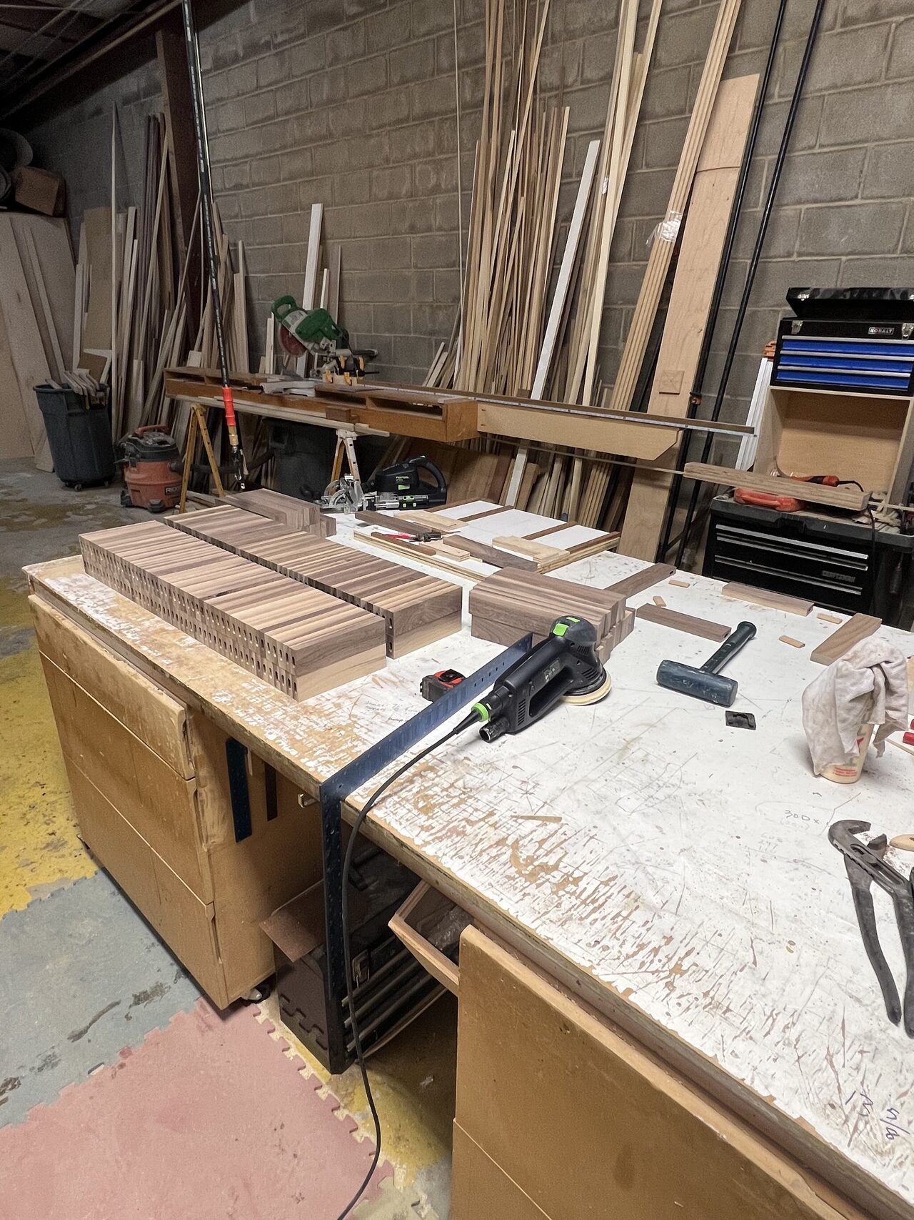 Work bench with cabinet parts, trim pieces, and layout tools staged for assembly for a Joel Hodge project.