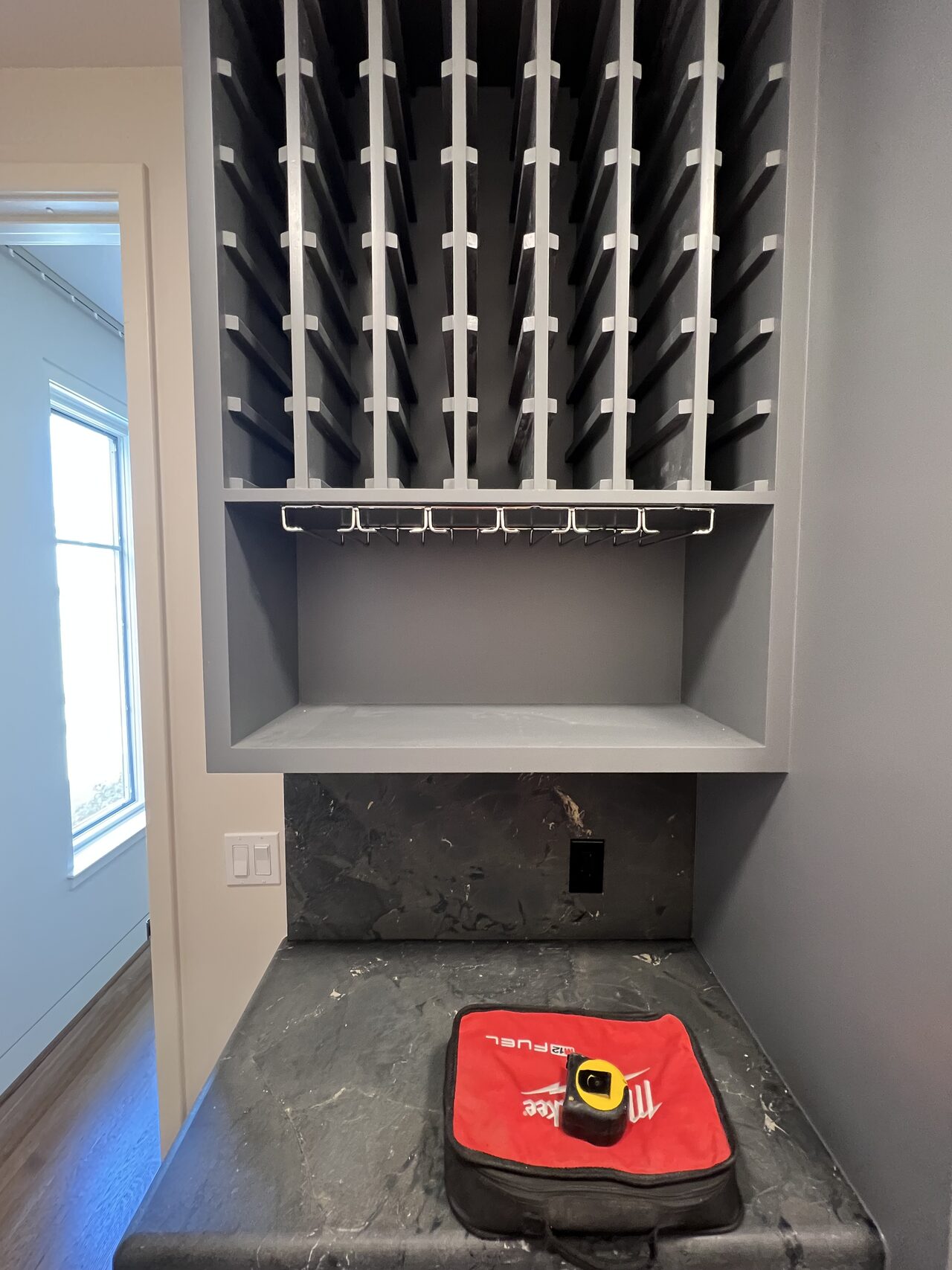 Installed wine storage cabinet with bottle grid, shelf, and lower opening fitted in the room for a Joel Hodge project.