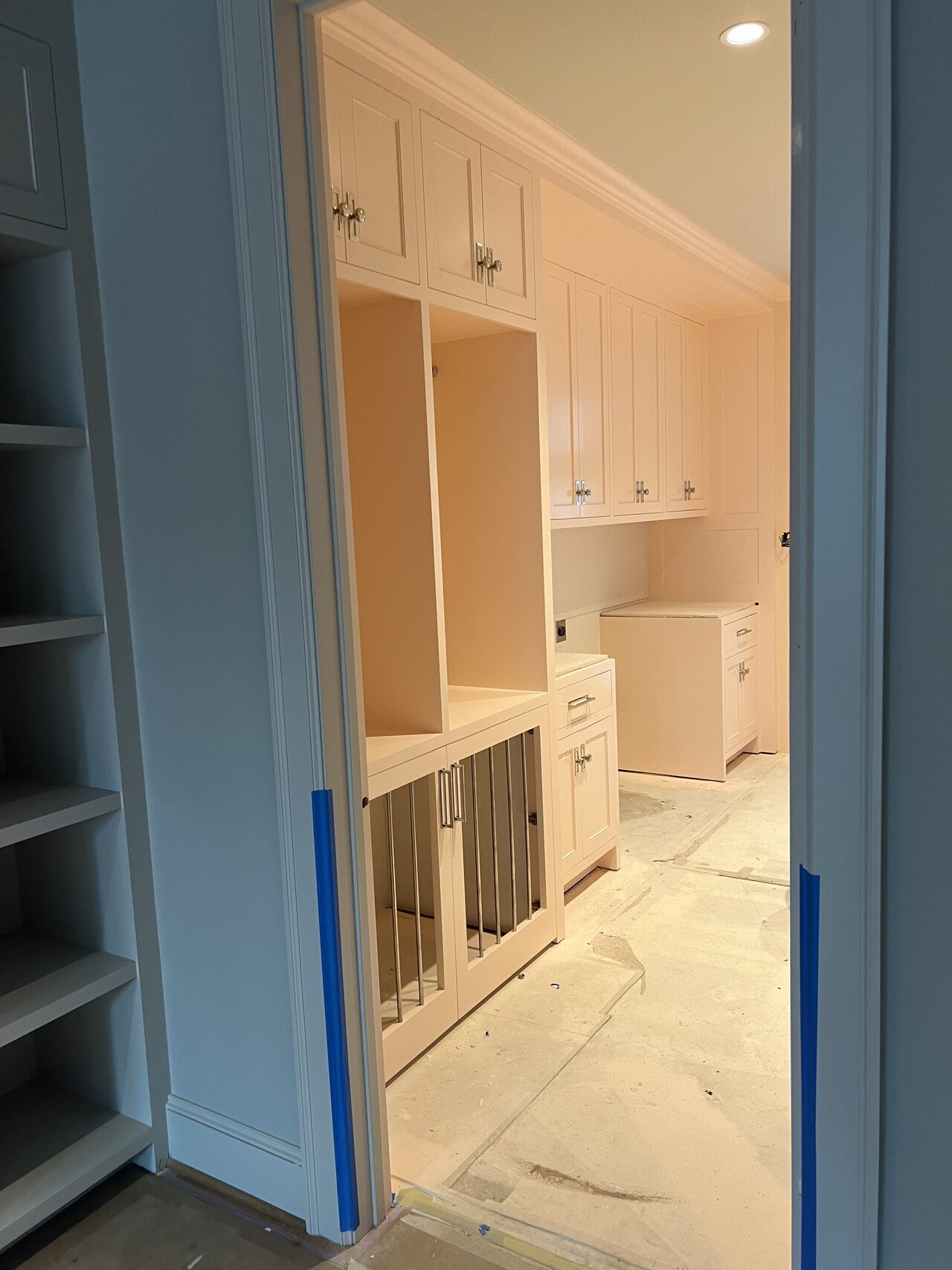 White built-in viewed from the doorway with tall shelves, base storage, and protected floors for a Joel Hodge project.