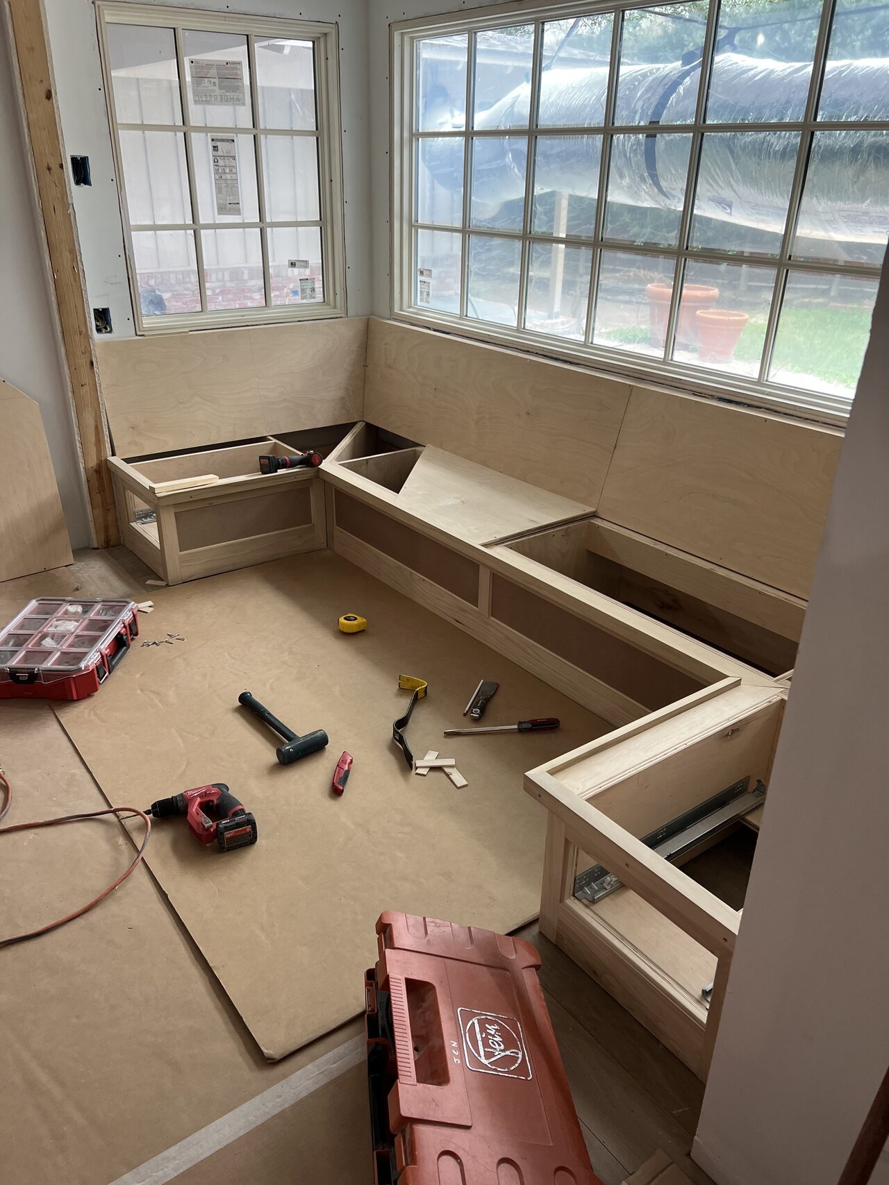 Window-seat base cabinets installed below the large window with tools and protection still in place for a Joel Hodge project.