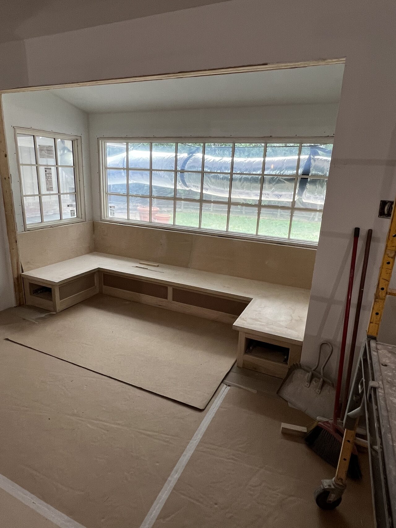 Wide room view showing the built-in bench under the window and floor protection during installation for a Joel Hodge project.