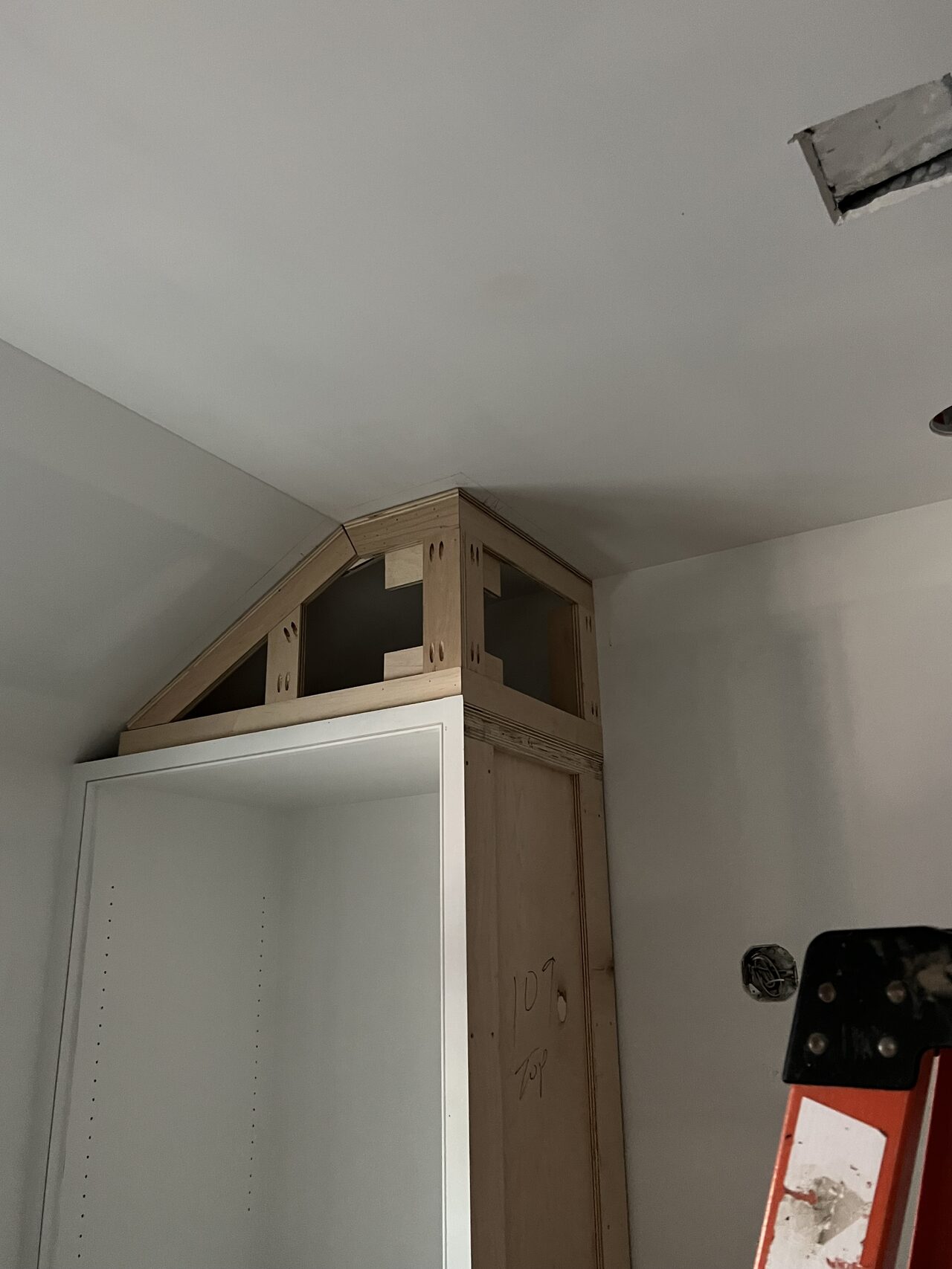 Upper niche cabinet frame being fitted into the wall opening with ladder access nearby for a Joel Hodge project.